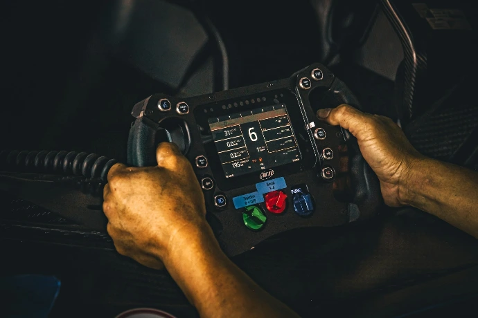 Oily hands hold a professional racing steering wheel.